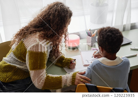 Candid shot of little Black boy and supportive mother engaged in hand drawing with colorful felt tip pens, while sitting together at desk in kids room Candid shot of little Black boy and supportive mother engaged in hand drawing with colorful felt tip pens, while sitting together at desk in kids room 120223935