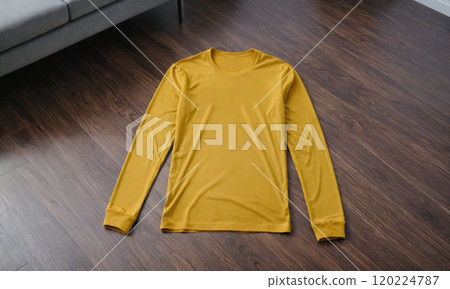 A yellow long-sleeved shirt lies flat on a wooden floor 120224787