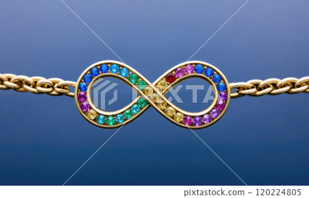 A close-up of a gold infinity bracelet adorned with colorful gemstones on a blue background 120224805