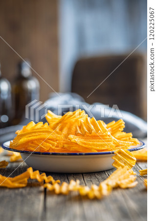 Crispy potato chips on plate on wooden table. 120225067