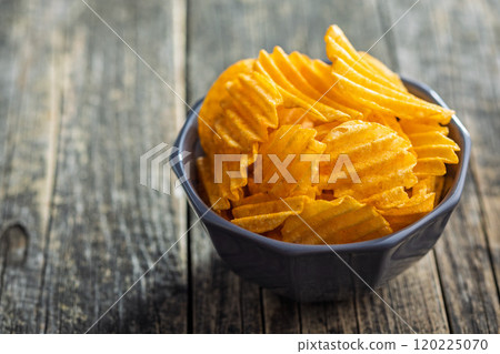 Crispy potato chips in bowl on wooden table. 120225070