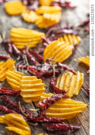 Crispy potato chips and chili peppers on wooden table. Crispy potato chips and chili peppers on wooden table. 120225073