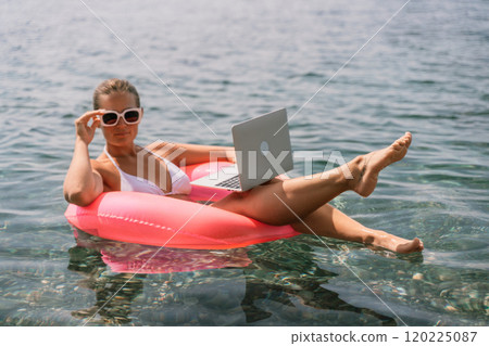A woman is floating in a pink inflatable raft with a laptop in her hand. She is smiling and she is enjoying her time in the water. A woman is floating in a pink inflatable raft with a laptop in her hand. She is smiling and she is enjoying her time in the water. 120225087