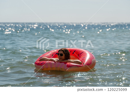 Woman Watermelon Float Summer Beach - A woman floats on a watermelon-shaped raft in the ocean on a sunny summer day. 120225099