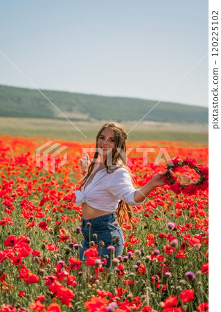 Happy woman in a poppy field in a white shirt and denim skirt with a wreath of poppies on her head posing and enjoying the poppy field. Happy woman in a poppy field in a white shirt and denim skirt with a wreath of poppies on her head posing and enjoying the poppy field. 120225102