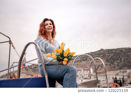 A woman is sitting on a boat with a bouquet of yellow flowers. The scene is set in a harbor with several boats in the background. The woman is enjoying the view and the peaceful atmosphere. 120225139