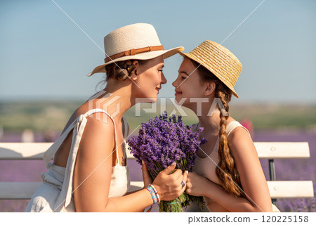 A woman and a child are sitting on a bench in a field of purple flowers lavande. The woman is holding a bouquet of flowers and the child is holding a bouquet of flowers as well 120225158