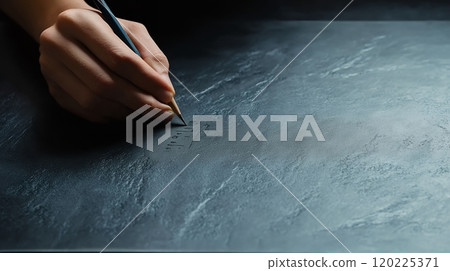 A hand writing on a dark slate surface with a pencil, illustrating creativity and focus in a minimalist setting 120225371