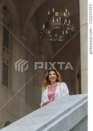 Woman Smiling Chandelier Building - A woman in a white jacket smiles while standing on a stone staircase in front of a building with a chandelier hanging above. Woman Smiling Chandelier Building - A woman in a white jacket smiles while standing on a stone staircase in front of a building with a chandelier hanging above. 120225424