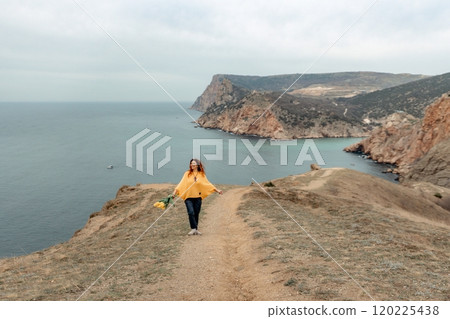 A woman is walking on a path near the ocean. She is carrying a bouquet of flowers. A woman is walking on a path near the ocean. She is carrying a bouquet of flowers. 120225438