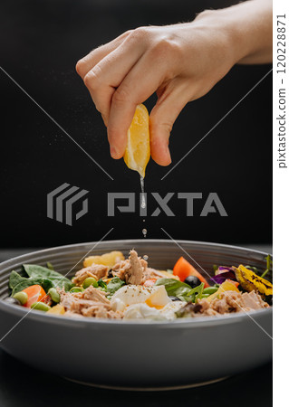 Fresh lemon juice squeezed over a nutritious tuna salad with poached egg, greens and vegetables 120228871
