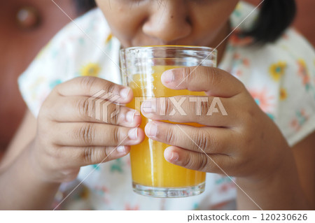 child hand holding a glass of orange juice child hand holding a glass of orange juice 120230626