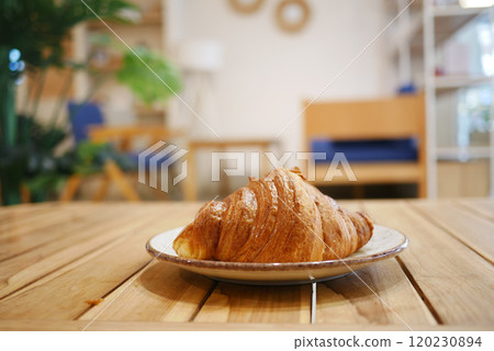 A Freshly Baked Croissant is beautifully presented on a rustic Wooden Table, ready to enjoy 120230894