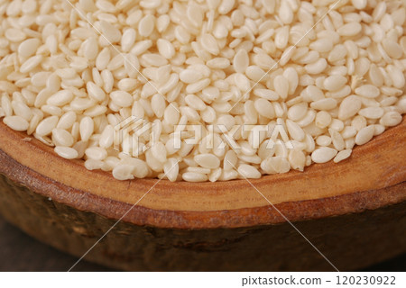 A closeup image showing raw white sesame seeds neatly displayed in a rustic wooden bowl 120230922