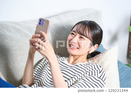 A young woman in casual clothes lying on a sofa, living room, smartphone A young woman in casual clothes lying on a sofa, living room, smartphone 120231344