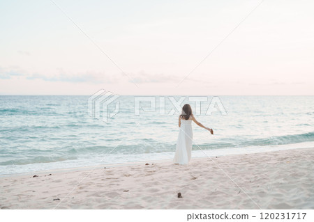Happy traveler woman in white dress enjoy beautiful sea view, young woman standing on sand and looking ocean at tropical beach. Freedom, relaxing, vacation holiday and summer travel concept 120231717