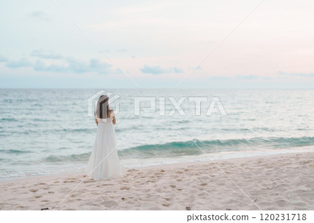 Happy traveler woman in white dress enjoy beautiful sea view, young woman standing on sand and looking ocean at tropical beach. Freedom, relaxing, vacation holiday and summer travel concept 120231718