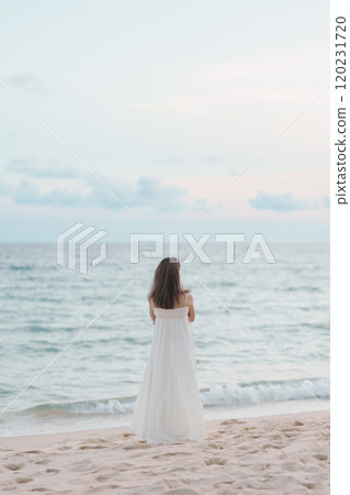 Happy traveler woman in white dress enjoy beautiful sea view, young woman standing on sand and looking ocean at tropical beach. Freedom, relaxing, vacation holiday and summer travel concept 120231720