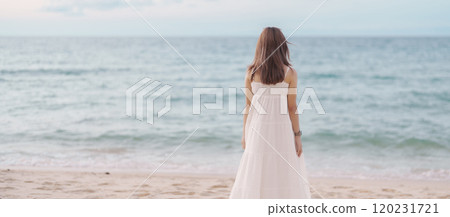 Happy traveler woman in white dress enjoy beautiful sea view, young woman standing on sand and looking ocean at tropical beach. Freedom, relaxing, vacation holiday and summer travel concept 120231721