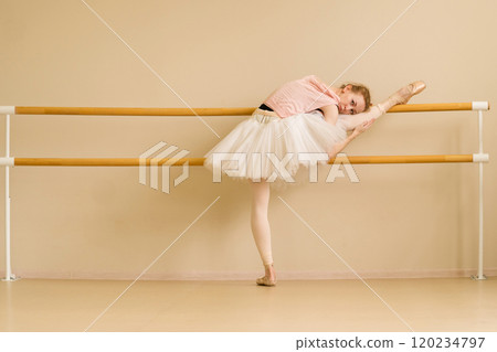 Ballet dancer rests on barre, holding stretch with leg raised 120234797