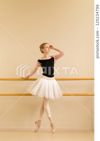 Focused ballerina stands gracefully on pointe, holding barre 120234798