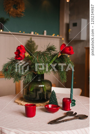Table with candle, and green vase with red flowers in dining room decorated for Christmas 120234987