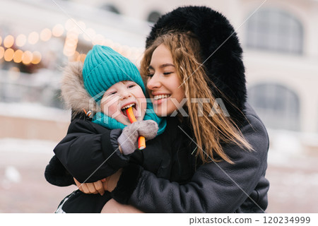 Young mother is holding boy and they are both smiling. The child is holding candy 120234999
