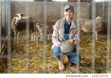 Portrait of female farm worker feeding lambs Portrait of female farm worker feeding lambs 120235135