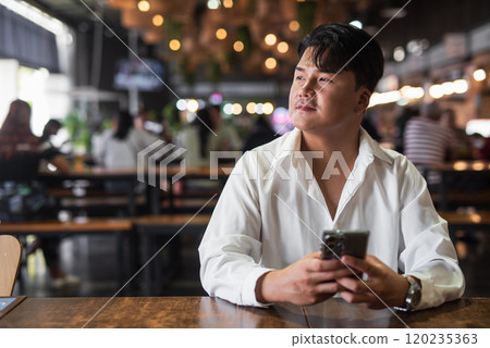 Portrait of Handsome Young Asian Man Sitting in Coffee Shop Restaurant 120235363