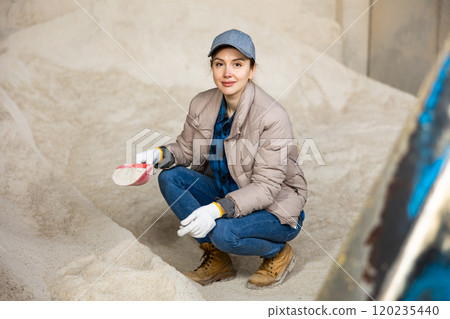 Woman using scoop to collect corn flour in an animal feed warehouse 120235440