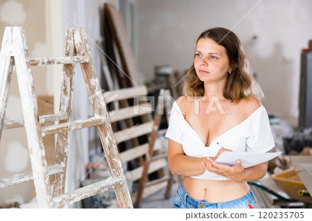 Woman with documents in her hands checks the quality of the completed repairs in cottage room Woman with documents in her hands checks the quality of the completed repairs in cottage room 120235705