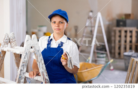 Portrait of positive builder woman in blue overalls next to stepladder Portrait of positive builder woman in blue overalls next to stepladder 120235819