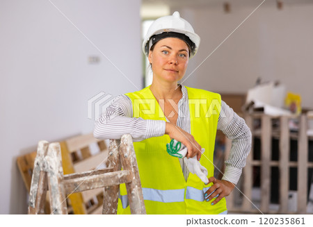 Confident female builder in vest and hard hat standing at construction site Confident female builder in vest and hard hat standing at construction site 120235861