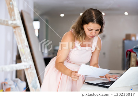 Female owner of cottage checks the completion of repair work using laptop 120236017