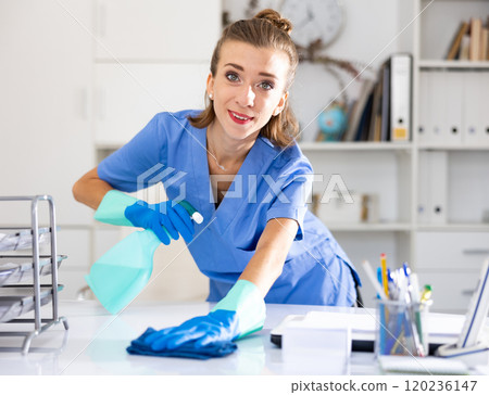 Positive woman cleaner polishing table in office 120236147