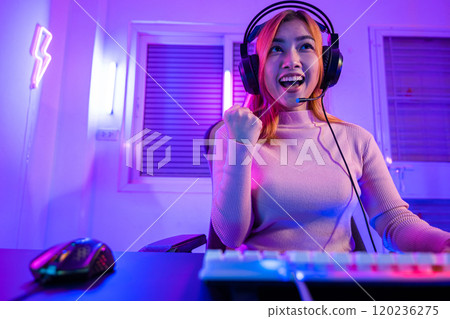 Winning Victory. Asian gamer playing online video game excited on desktop computer PC with purple light on night, Happy woman in gaming headphones use computer she successful, E-Sport concept Winning Victory. Asian gamer playing online video game excited on desktop computer PC with purple light on night, Happy woman in gaming headphones use computer she successful, E-Sport concept 120236275
