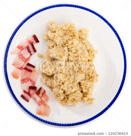 There is portion of boiled oatmeal porridge with pieces of salted bacon on plate. There is portion of boiled oatmeal porridge with pieces of salted bacon on plate. 120236423