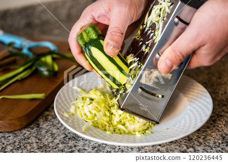 Mens hands hold piece of ripe zucchini and chop vegetables with grater 120236445