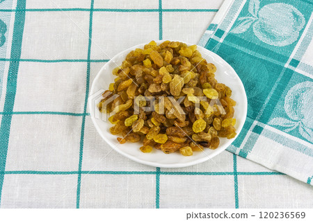 On a textile tablecloth there is a saucer with raisins On a textile tablecloth there is a saucer with raisins 120236569