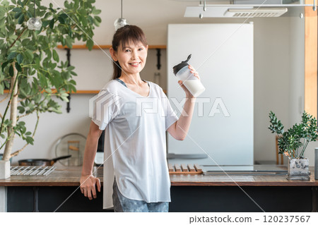 Young Asian woman drinking protein and EAA after training in the living room at home 120237567