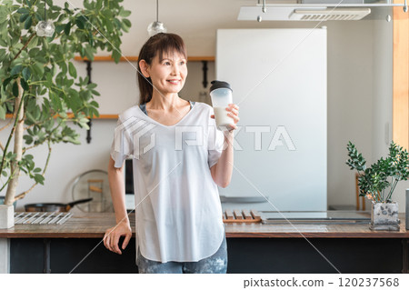 Young Asian woman drinking protein and EAA after training in the living room at home 120237568