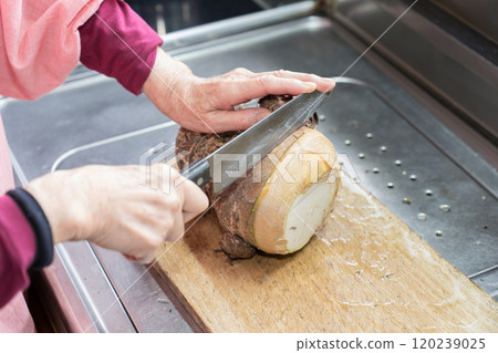 A senior woman cutting taro root with a knife 120239025