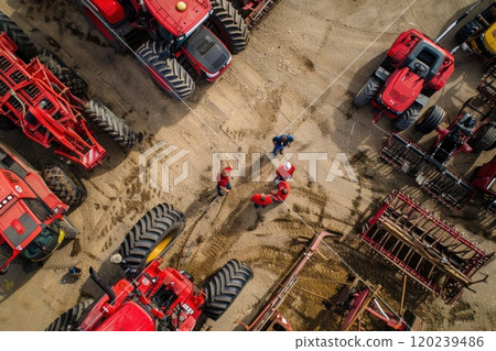 An aerial view of four red tractors parked in a lot with four people standing near the center. 120239486