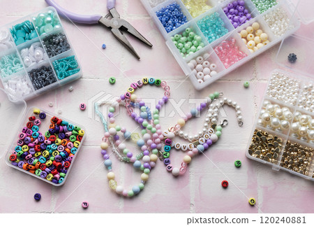 Colorful beads and jewelry making tools arranged on pink tile surface 120240881