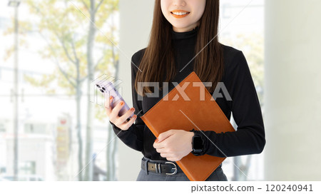 Smiling woman/businesswoman holding a smartphone and a binder Smiling woman/businesswoman holding a smartphone and a binder 120240941