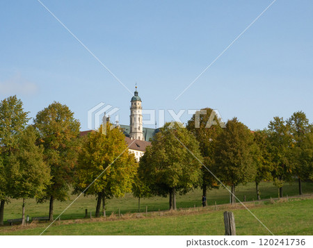 Neresheim, Germany - September 30th 2023: The church tower of the famous monastery behind colourful trees 120241736