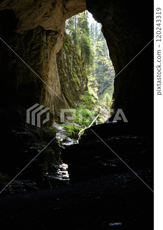 Silhouette of a big cave entrance from inside, water stream flowing into cave 120243319