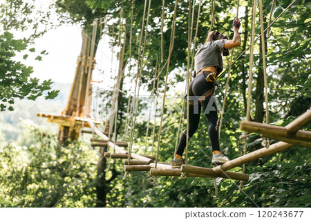 A woman skillfully navigating a challenging tree climbing course while surrounded by vibrant and lush greenery 120243677