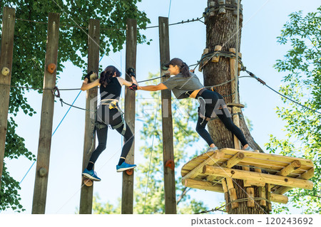 Two girls skillfully navigate a challenging high ropes course, showcasing their teamwork and spirit of adventure Two girls skillfully navigate a challenging high ropes course, showcasing their teamwork and spirit of adventure 120243692