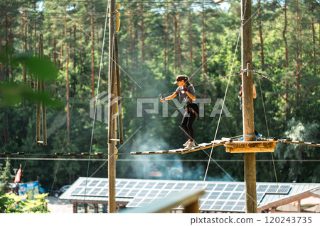 A skilled individual expertly navigating a challenging high ropes course surrounded by vibrant, lush greenery A skilled individual expertly navigating a challenging high ropes course surrounded by vibrant, lush greenery 120243735